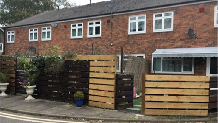 A row of red brick houses with wooden fence panels in front of them.